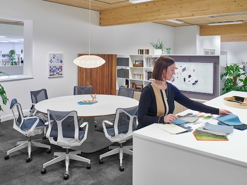 An employee searches through material swatches in a meeting seating featuring Cosm Chairs around a Megaped Table.