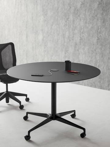 A round Civic Table in graphite with central power access and a graphite Cosm Chair positioned alongside.