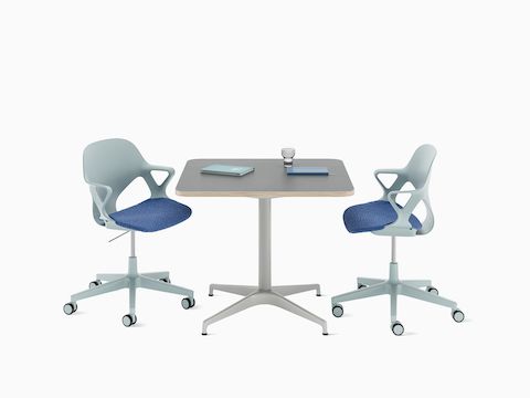 A front view of a Civic Table with a Blue Zeph chair on either side and some notebooks on the table.