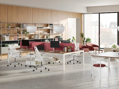 An office with open shelving along the back wall and options for dedicated workstations or team tables in the foreground. Additional ancillary seating areas are in the background.