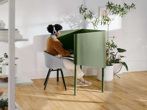 A woman sitting in a grey Hay About A Chair at a green OE1 Nook, with a grey OE1 Agile Wall with full shelves in the foreground.