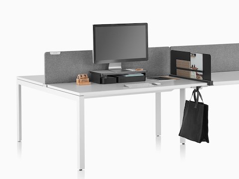A work surface equipped with Ubi Work Tools, including a black monitor platform shelf, slim screen, and bag hook.