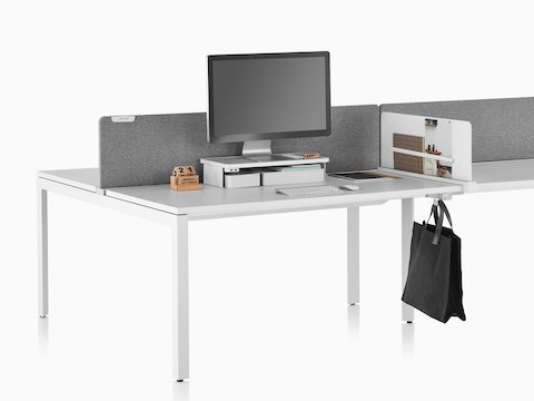 A work surface equipped with Ubi Work Tools, including a white monitor platform shelf, slim screen, and bag hook.