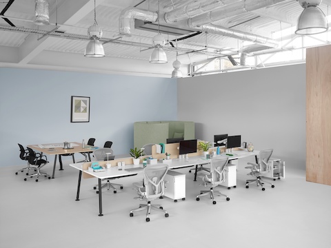 An open workplace with a meeting table, partially enclosed solo work area, and bench desking with light grey Aeron office chairs.