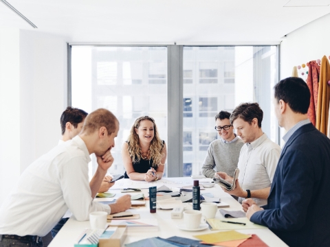 People gather around a conference table in a sunlit room to converse.