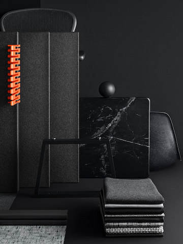 Stacks of folded grey, black, muted patterned textile samples on a dark grey table, with a black Metaform collborative space wall behind them.