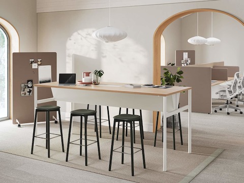 A bright office meeting room with an OE1 Communal Table and brown Bound Mobile Screen and workstations with brown Bound Screens and Cosm Chairs in the background.