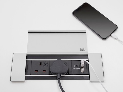 An open Power Frame Cover with an electrical plug and a mobile phone plugged in.