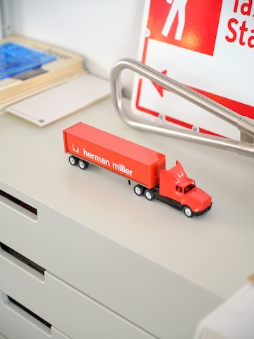 A toy truck with Herman Miller's signature red logo sits atop a grey filing cabinet.