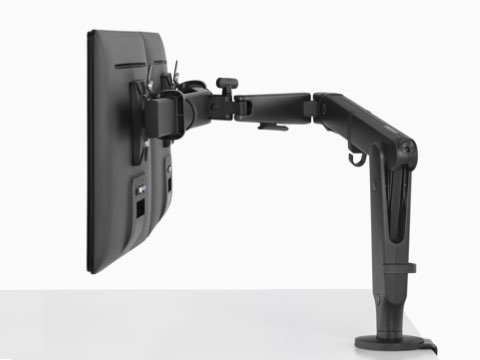 A side view of two monitors suspended above a white work surface from a black Ollin Monitor Arm.