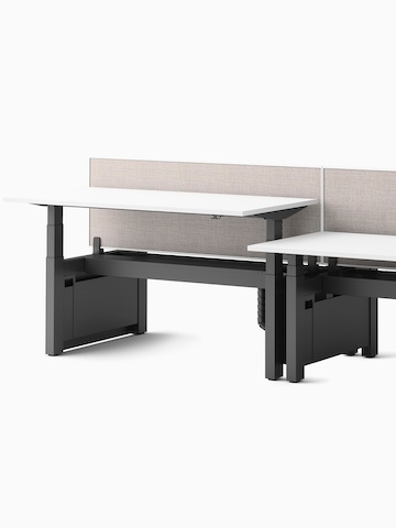 A cluster of four Ratio height-adjustable desks, positioned at seating and standing heights, attached side by side with framed, beige mounted privacy screens.