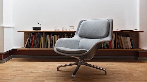 A grey Striad Lounge Chair in front of a bookshelf. Select to go to a WHY Magazine interview of designers Jürgen Laub and Markus Jehs.